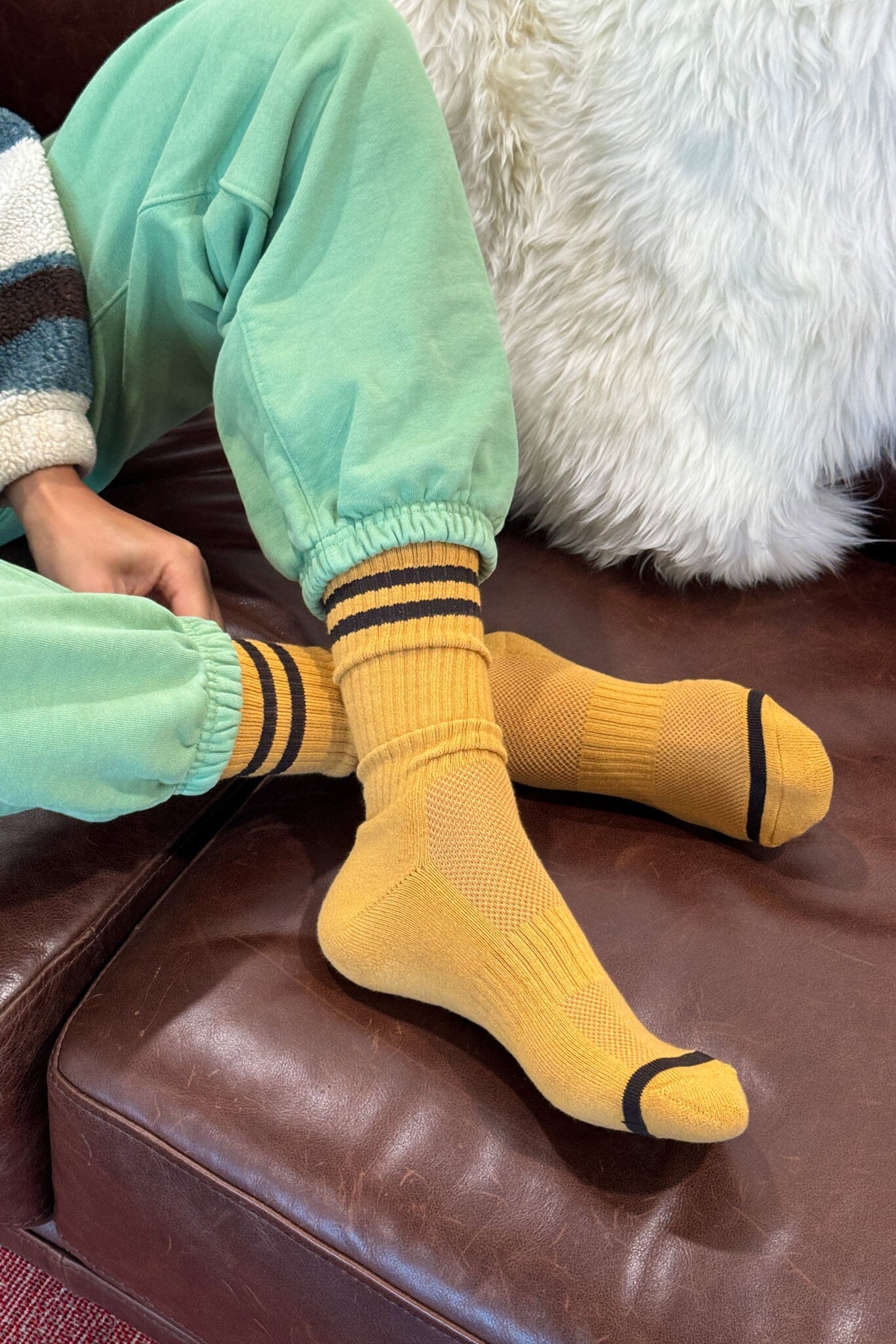 Person wearing yellow socks with black stripes on a brown couch.