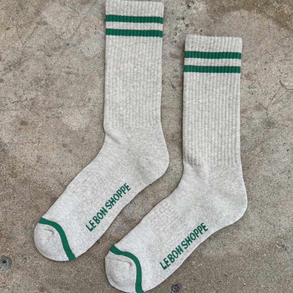 Two white socks with green stripes and 'Le Bon Shoppe' branding on a concrete surface.