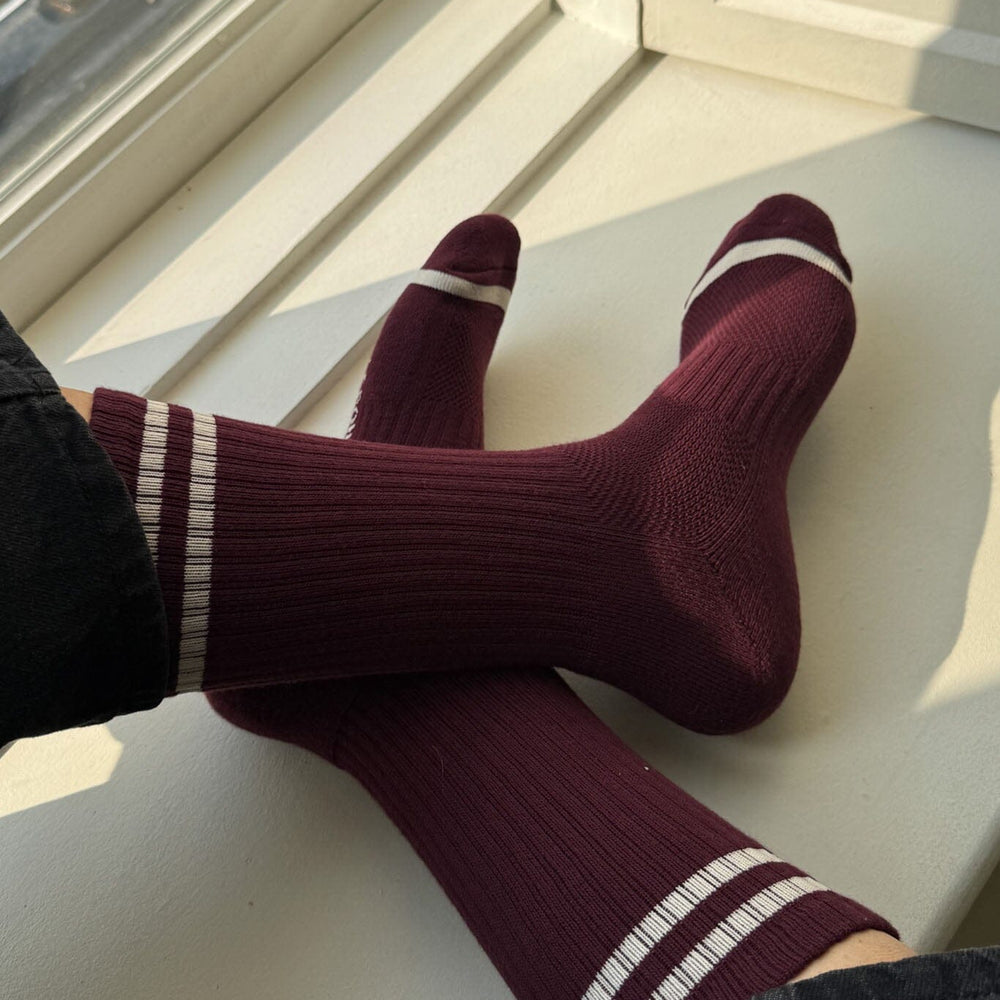 Maroon socks with white stripes on a white surface near a window.