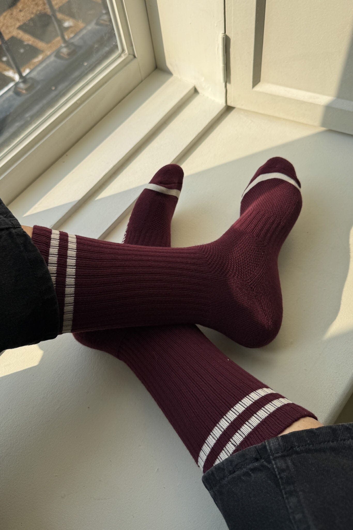 Maroon socks with white stripes on a white surface near a window.