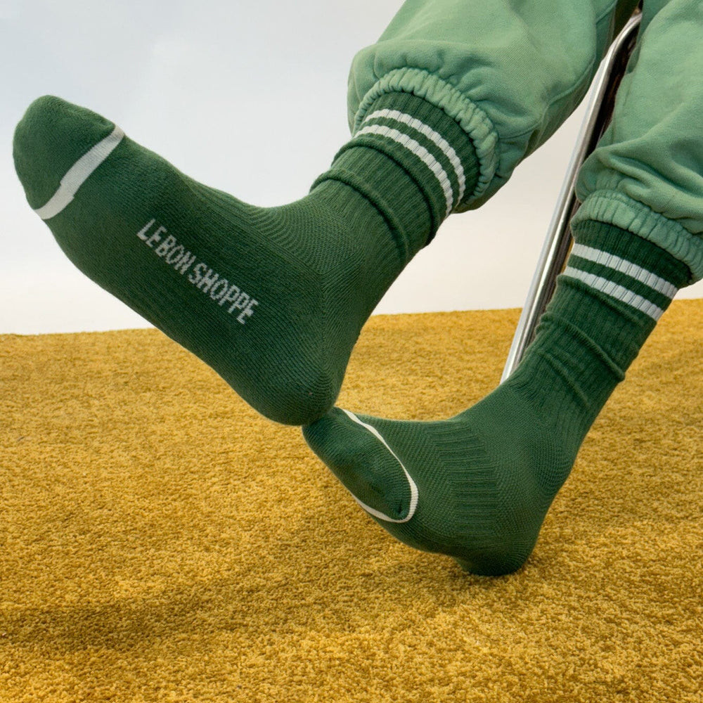 Green socks with white stripes and 'Le Bon Shoppe' branding on a yellow surface.