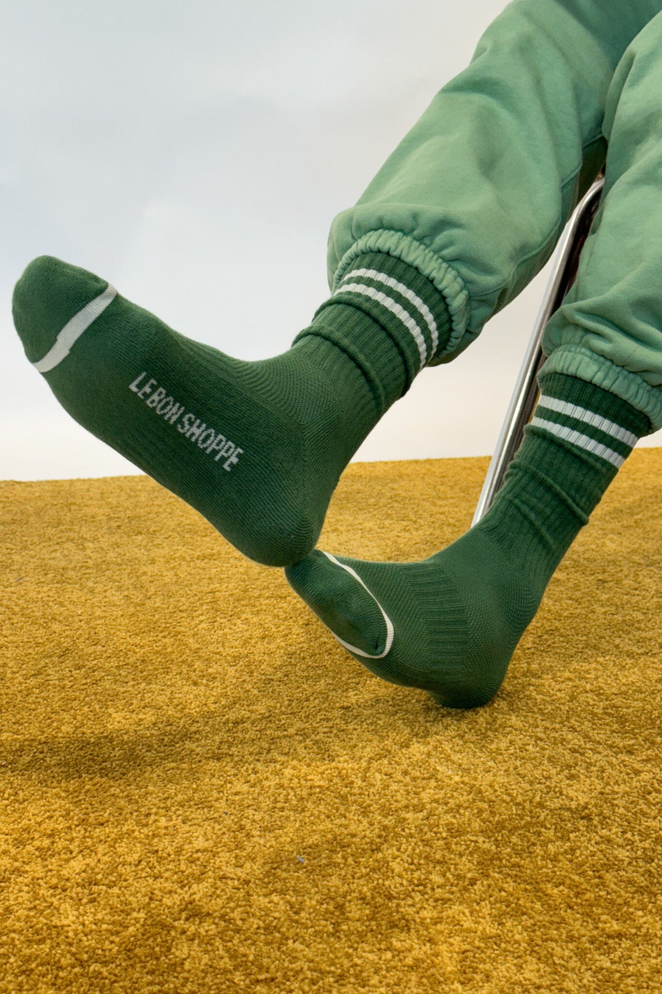 Green socks with white stripes and 'Le Bon Shoppe' branding on a yellow surface.