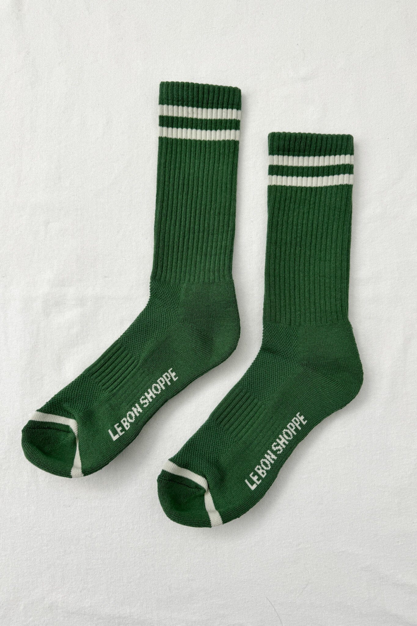 Green socks with white stripes and 'Le Bon Shoppe' branding on a light gray background