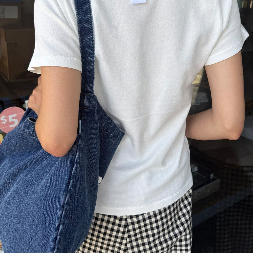 
                  
                    Person wearing a white t-shirt with a blue denim bag over one shoulder, standing indoors.
                  
                