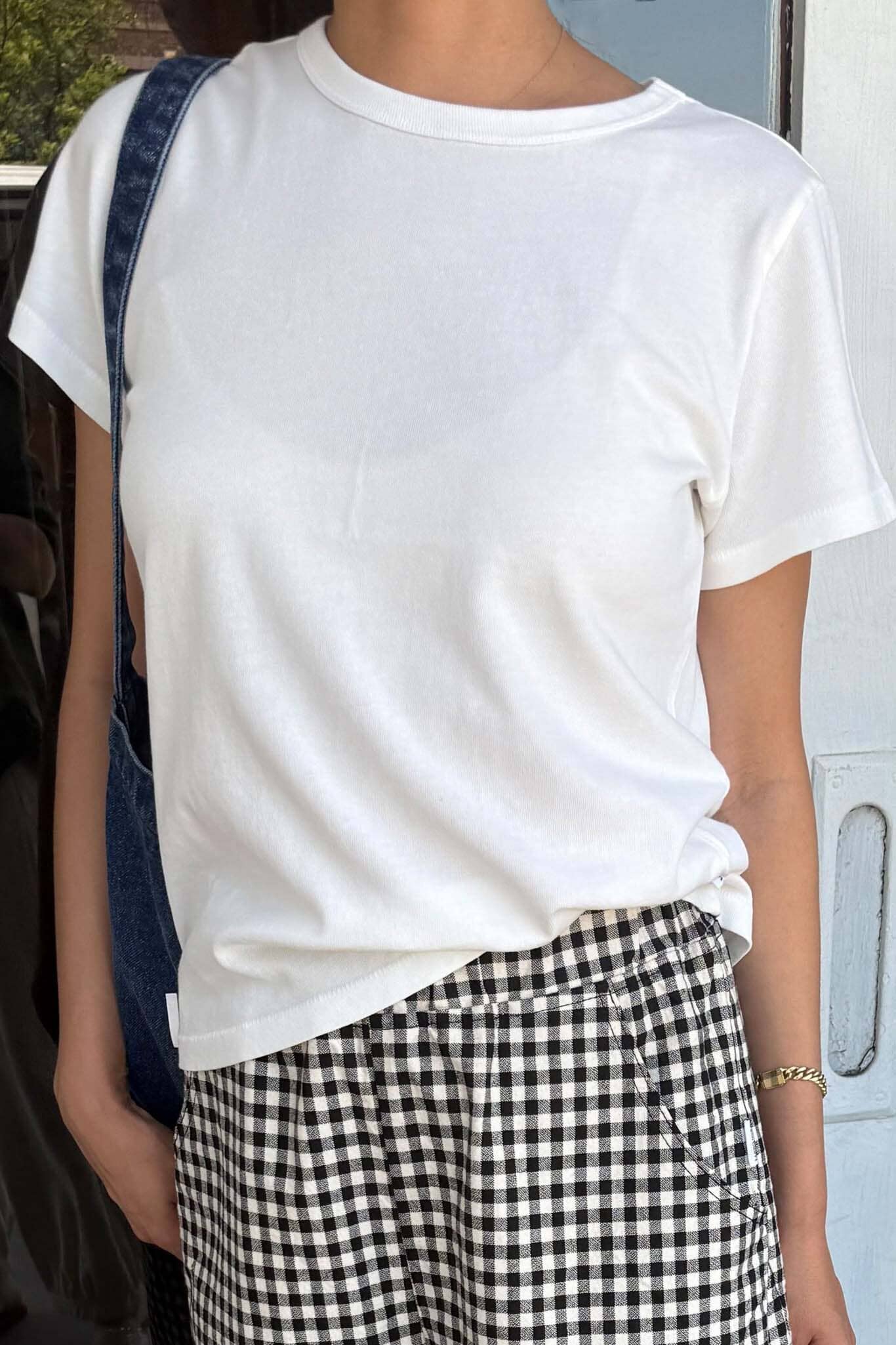 Person wearing a white t-shirt and checkered pants with a denim bag over one shoulder.
