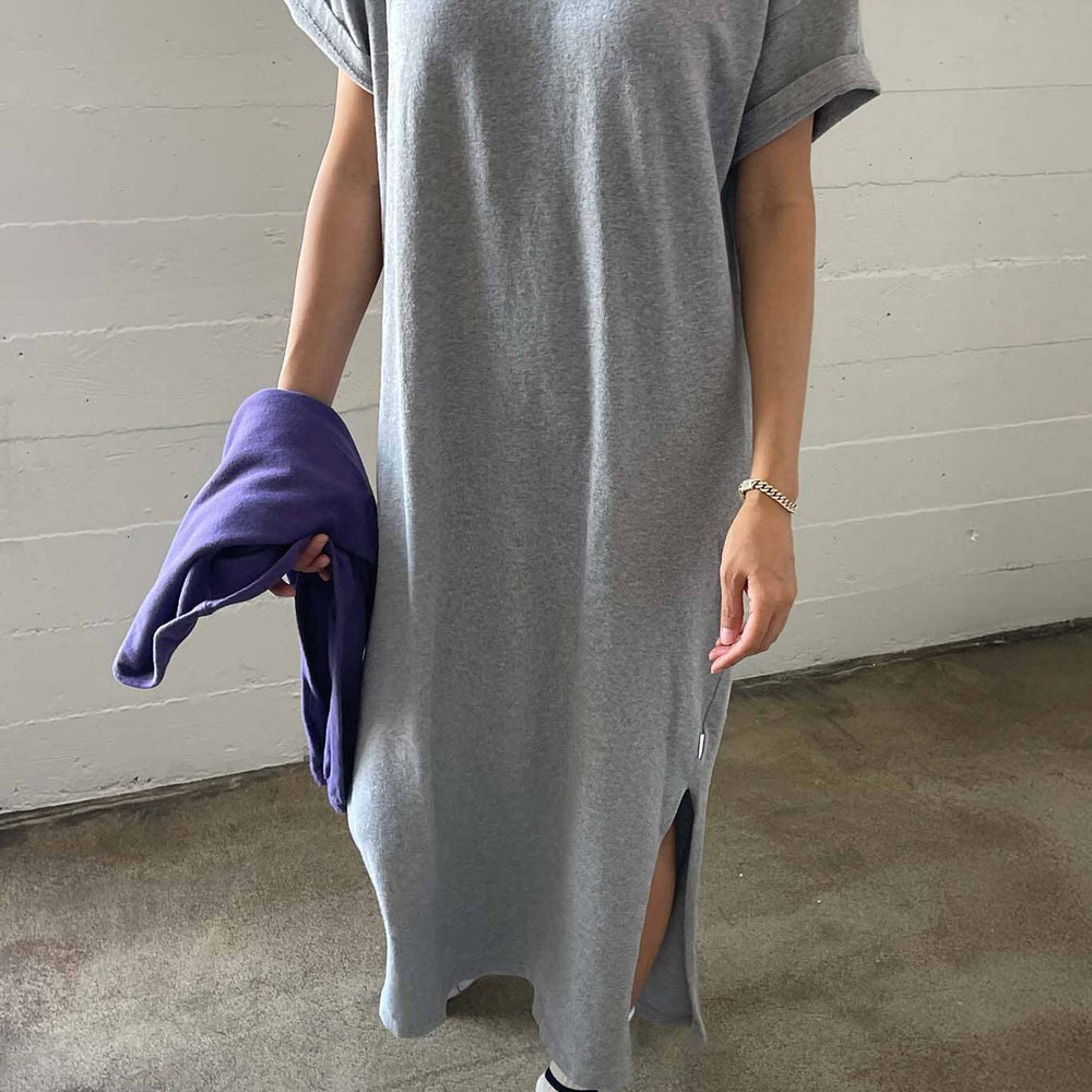 Person wearing a long gray t-shirt with a white wall background