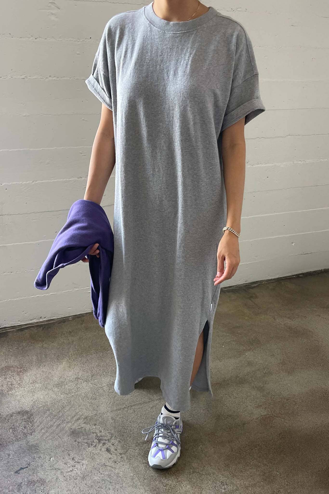 Person wearing a long gray t-shirt with a white wall background