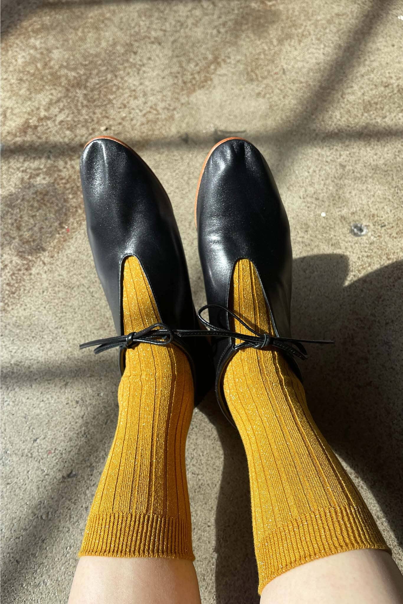 Black shoes with glitter yellow socks on a concrete surface