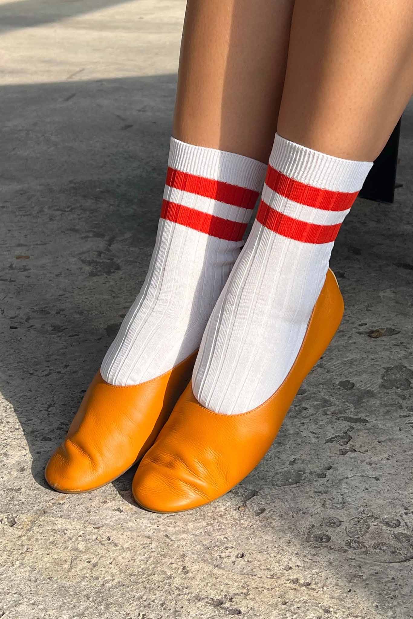 White socks with red stripes worn with orange shoes on a concrete surface