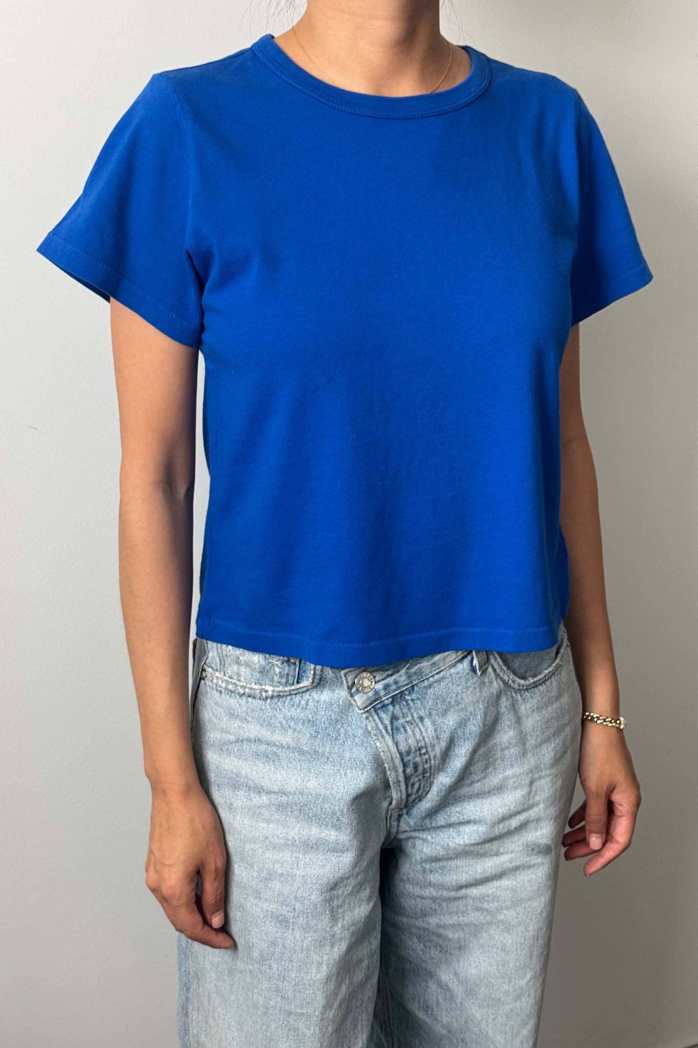 Person wearing a blue t-shirt and light blue jeans against a plain background