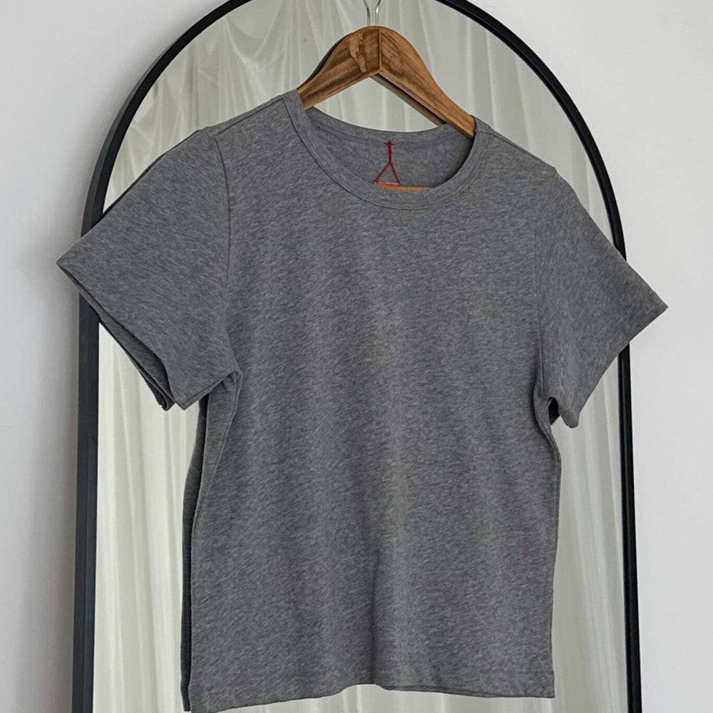 
                  
                    Gray t-shirt on a wooden hanger against a white curtain background
                  
                
