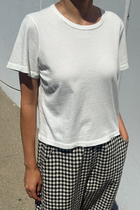 Person wearing a plain white t-shirt and checkered pants against a gray background