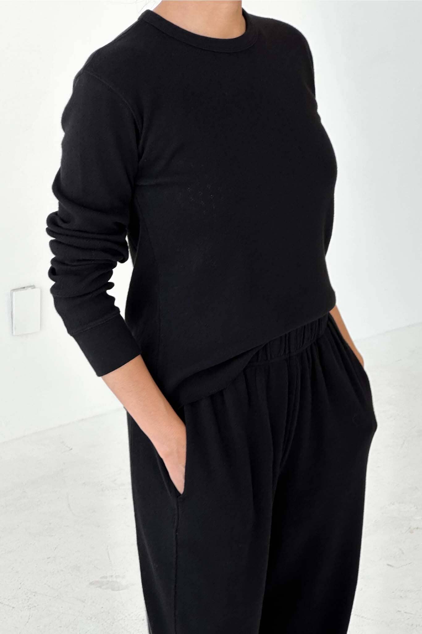 Person wearing a black sweater and black pants against a white background
