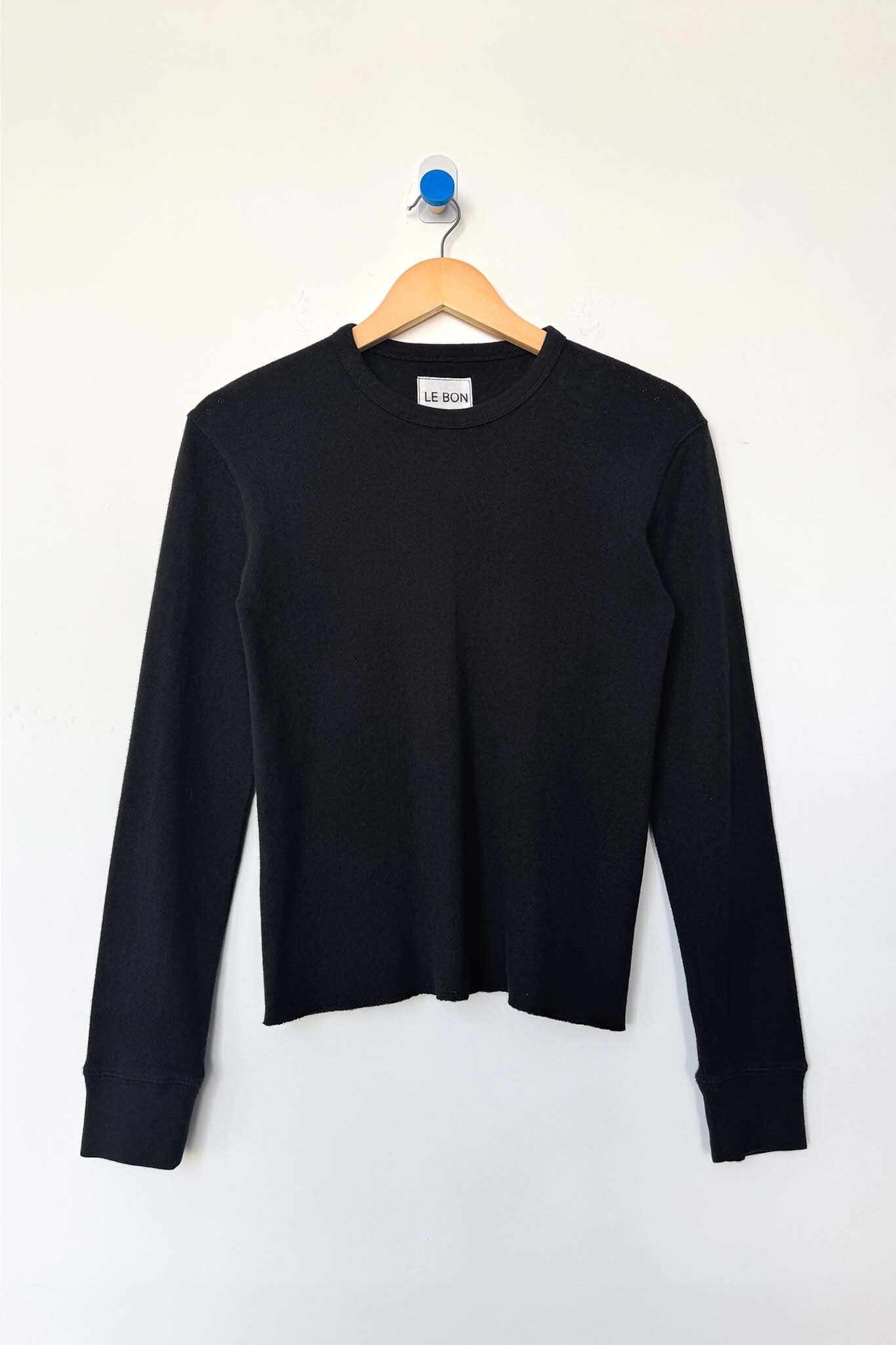 Black long-sleeve shirt on a wooden hanger against a white background