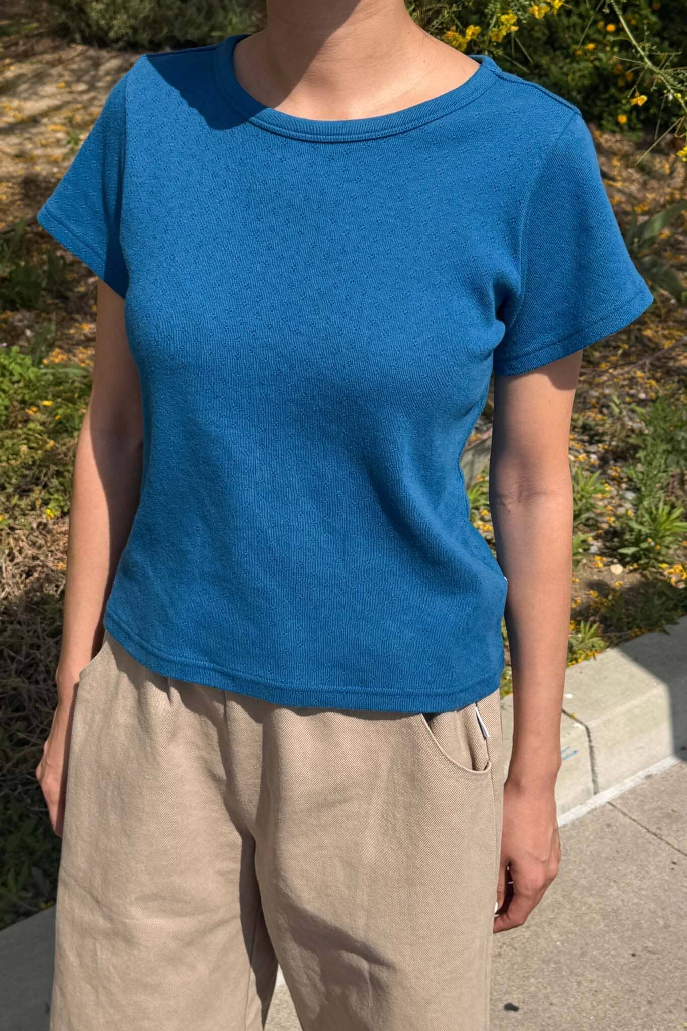 Person wearing a blue t-shirt and beige pants standing outdoors.