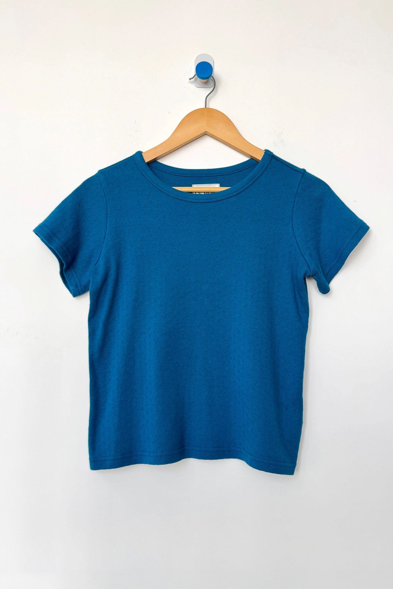 Blue t-shirt on a wooden hanger against a white background