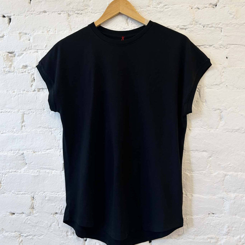 Black t-shirt on a wooden hanger against a white brick wall
