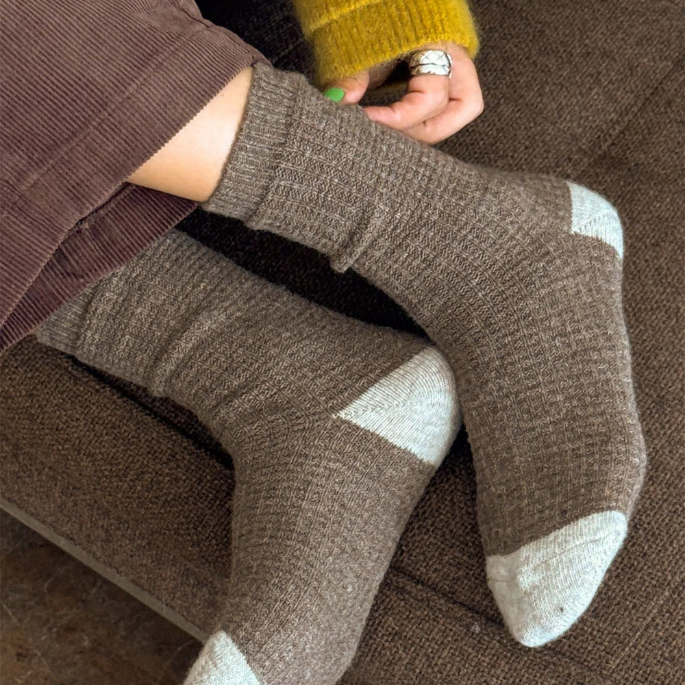 Person wearing brown socks with white accents on a brown couch.