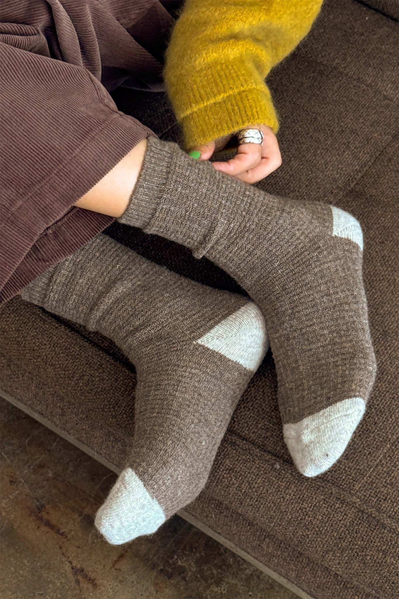 Person wearing brown socks with white accents on a brown couch.