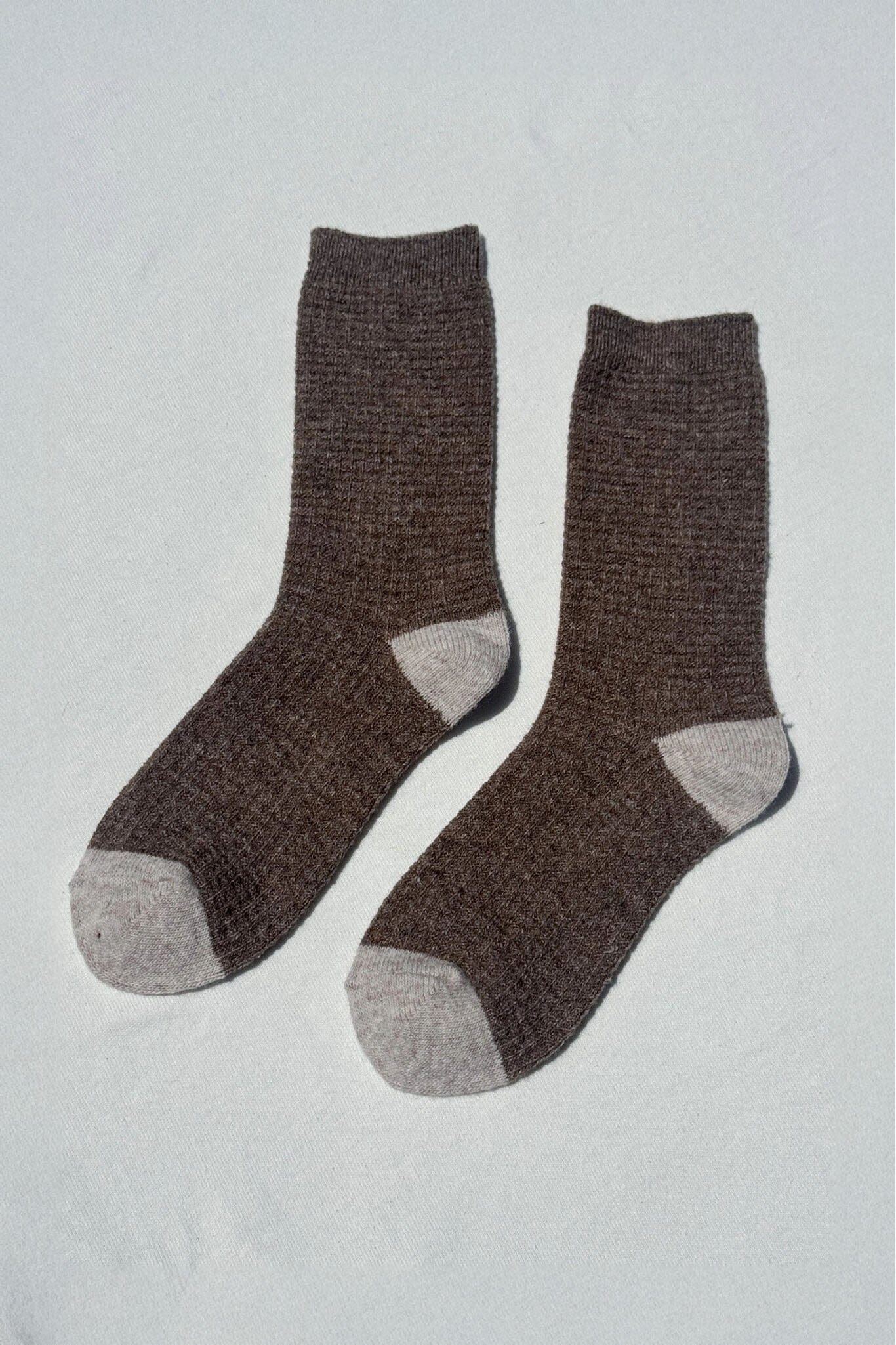 Pair of brown wool socks with gray toes and cuffs on a light gray background