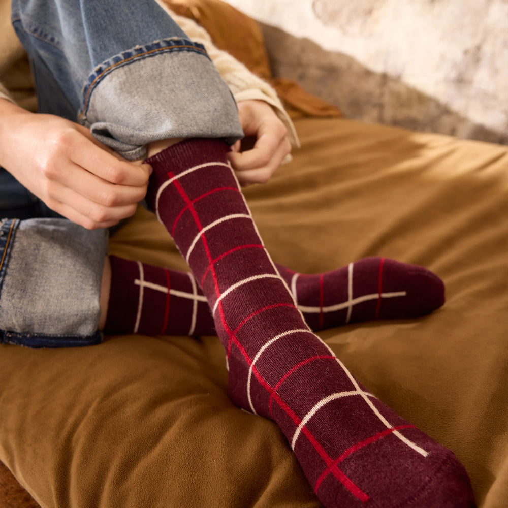 Person wearing burgundy plaid socks sitting on a brown surface.
