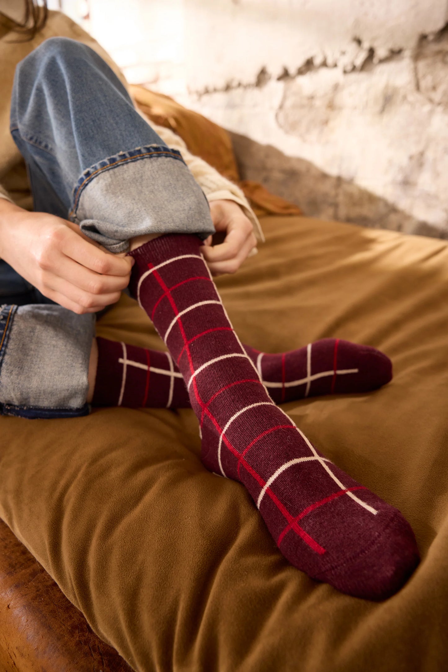 Person wearing burgundy plaid socks sitting on a brown surface.