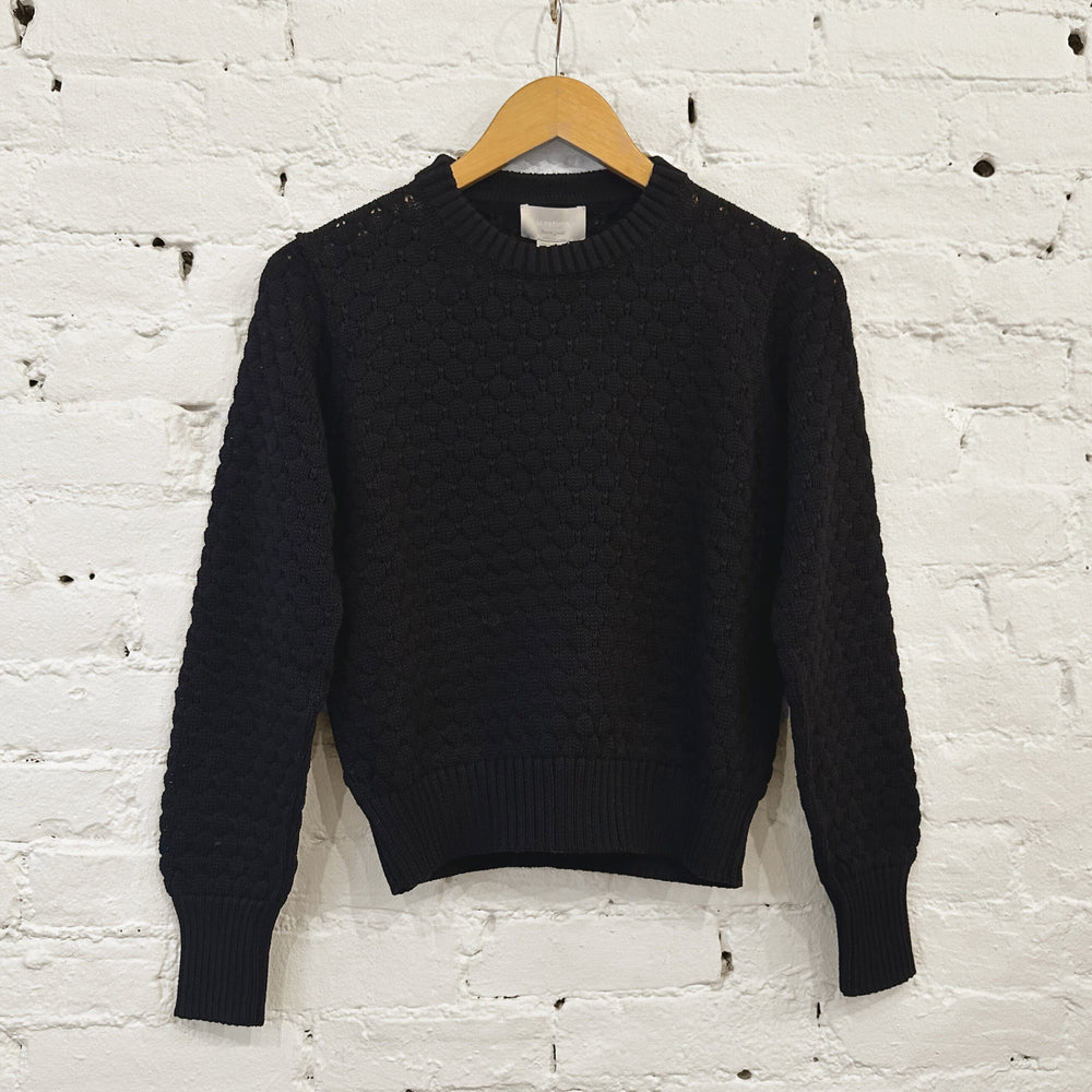 Black sweater on a wooden hanger against a white brick wall