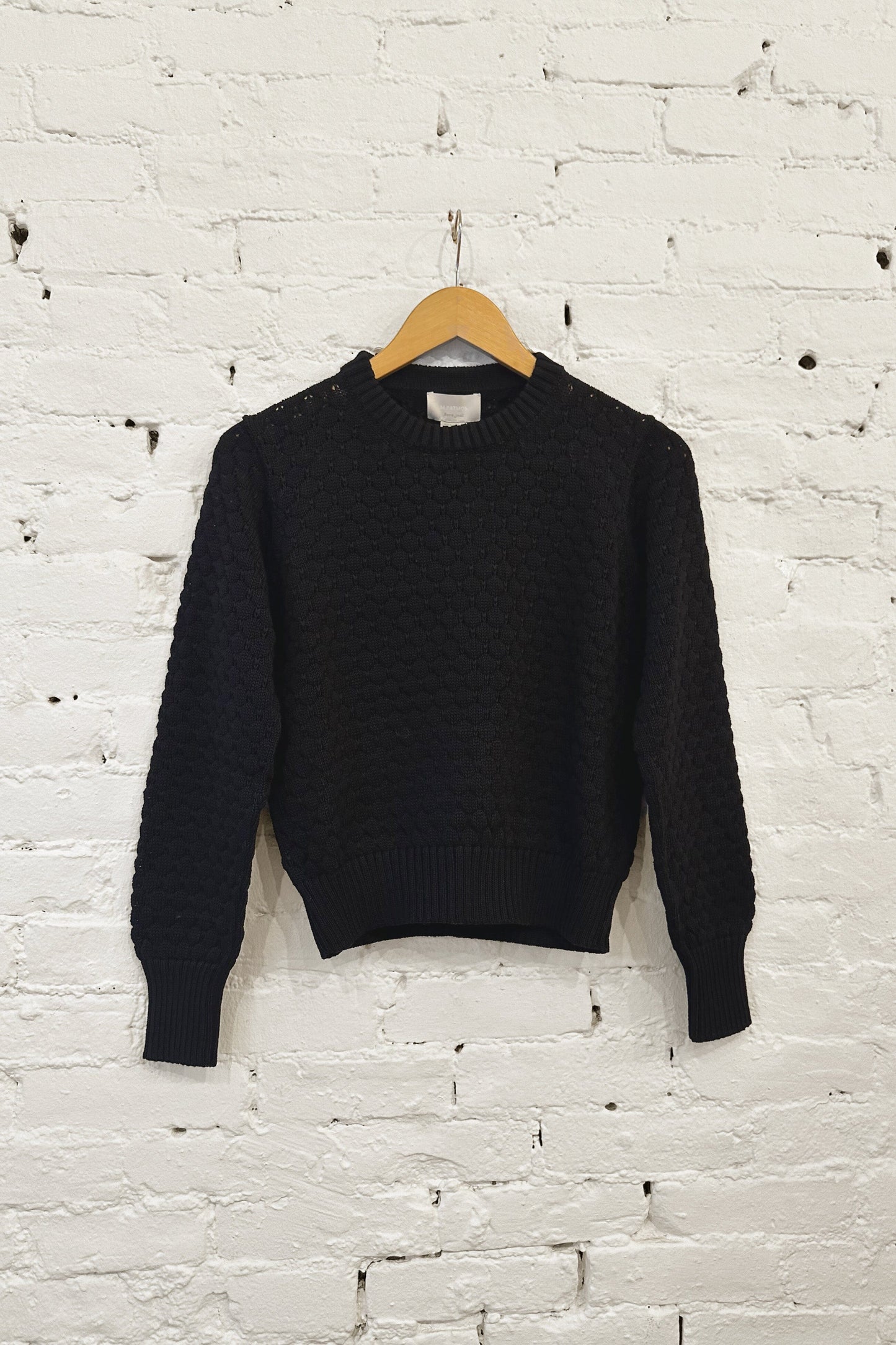 Black sweater on a wooden hanger against a white brick wall