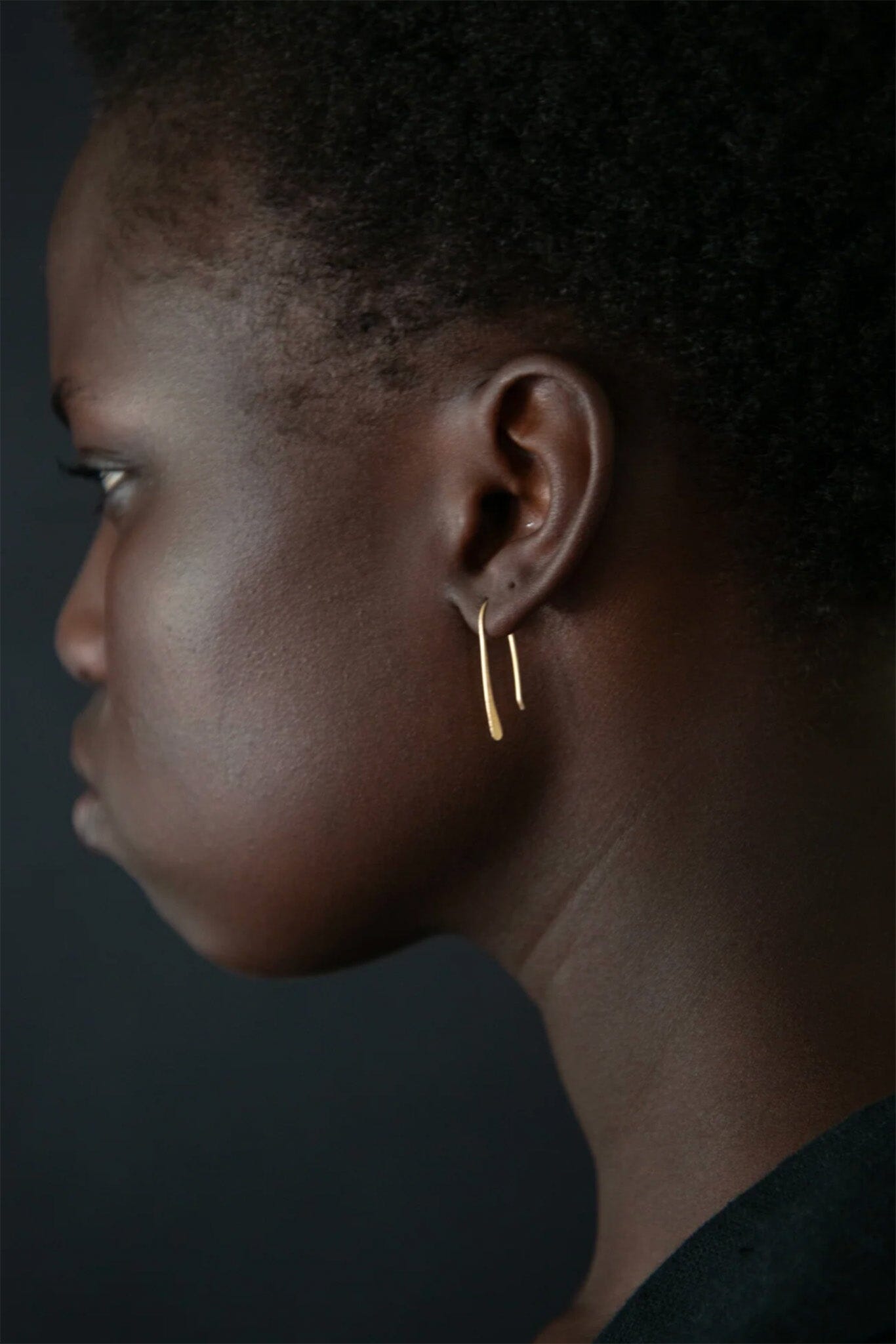 Profile of a person wearing a gold earring against a dark background