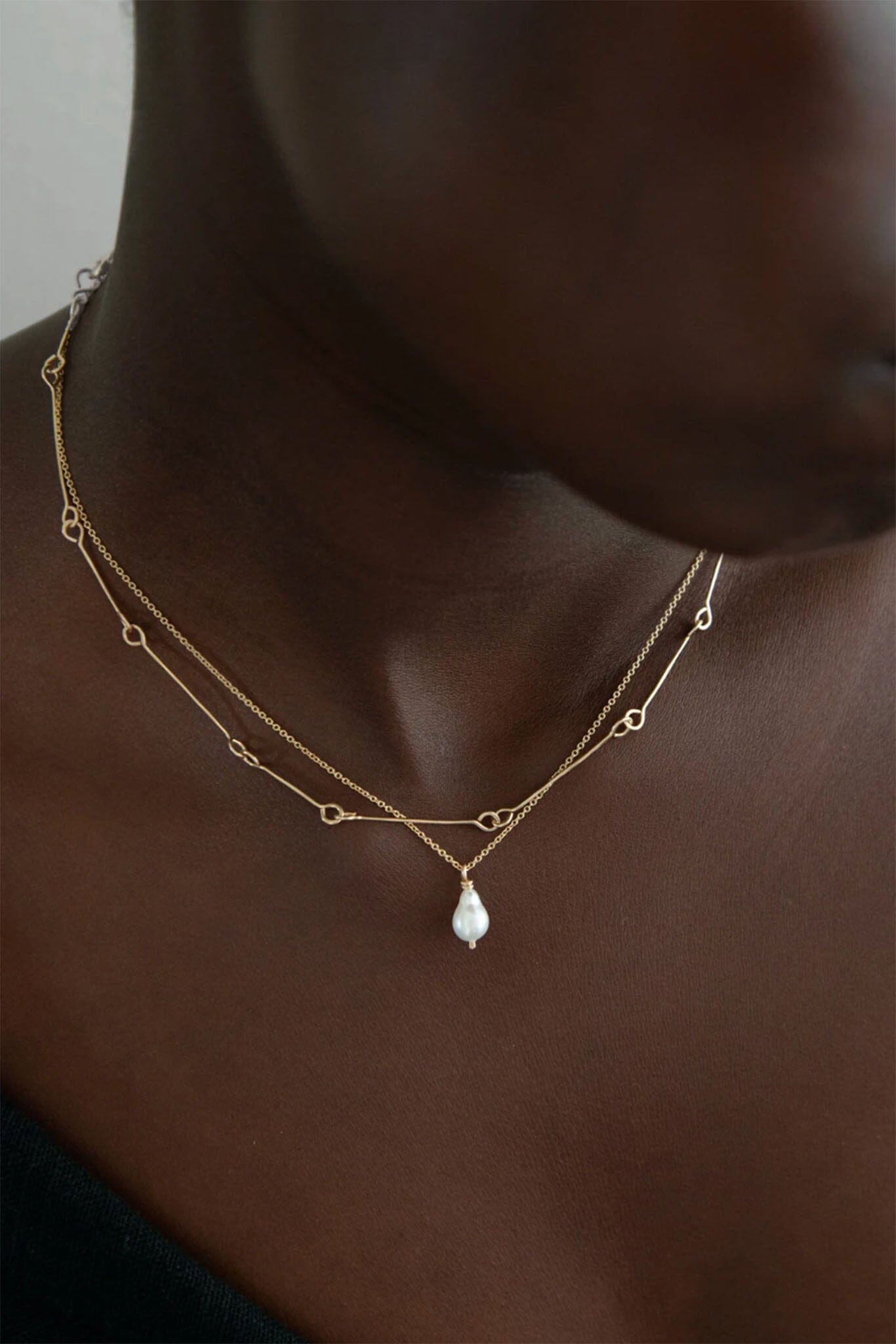 A woman stacks two gold necklaces, one gold chain and the other a white pearl necklace. 