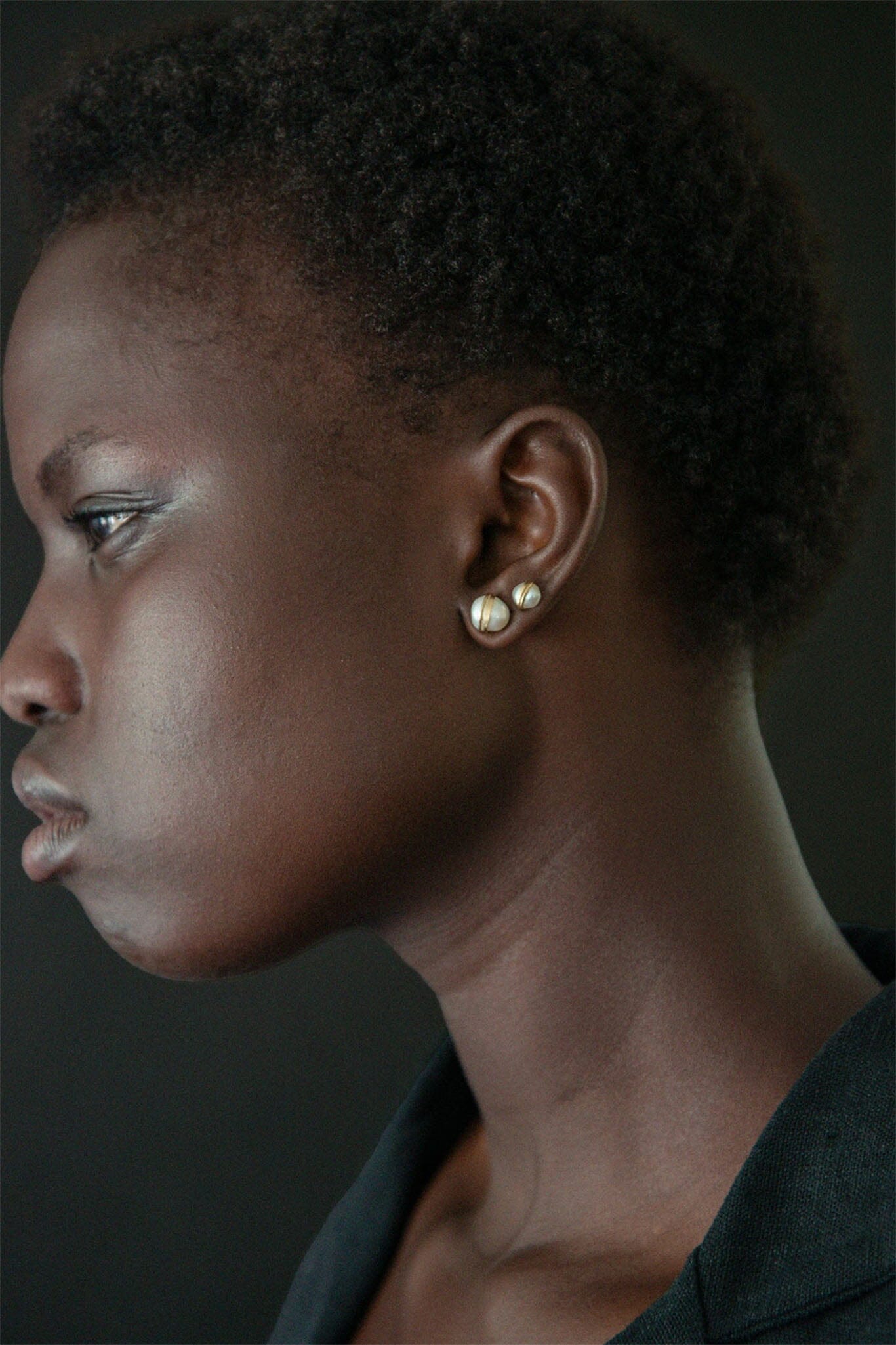 Profile of a woman wearing pearl earrings against a dark background