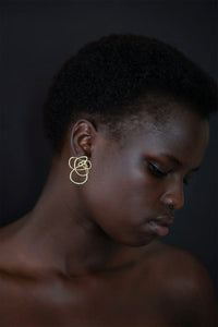 Woman wearing abstract gold earrings against a dark background