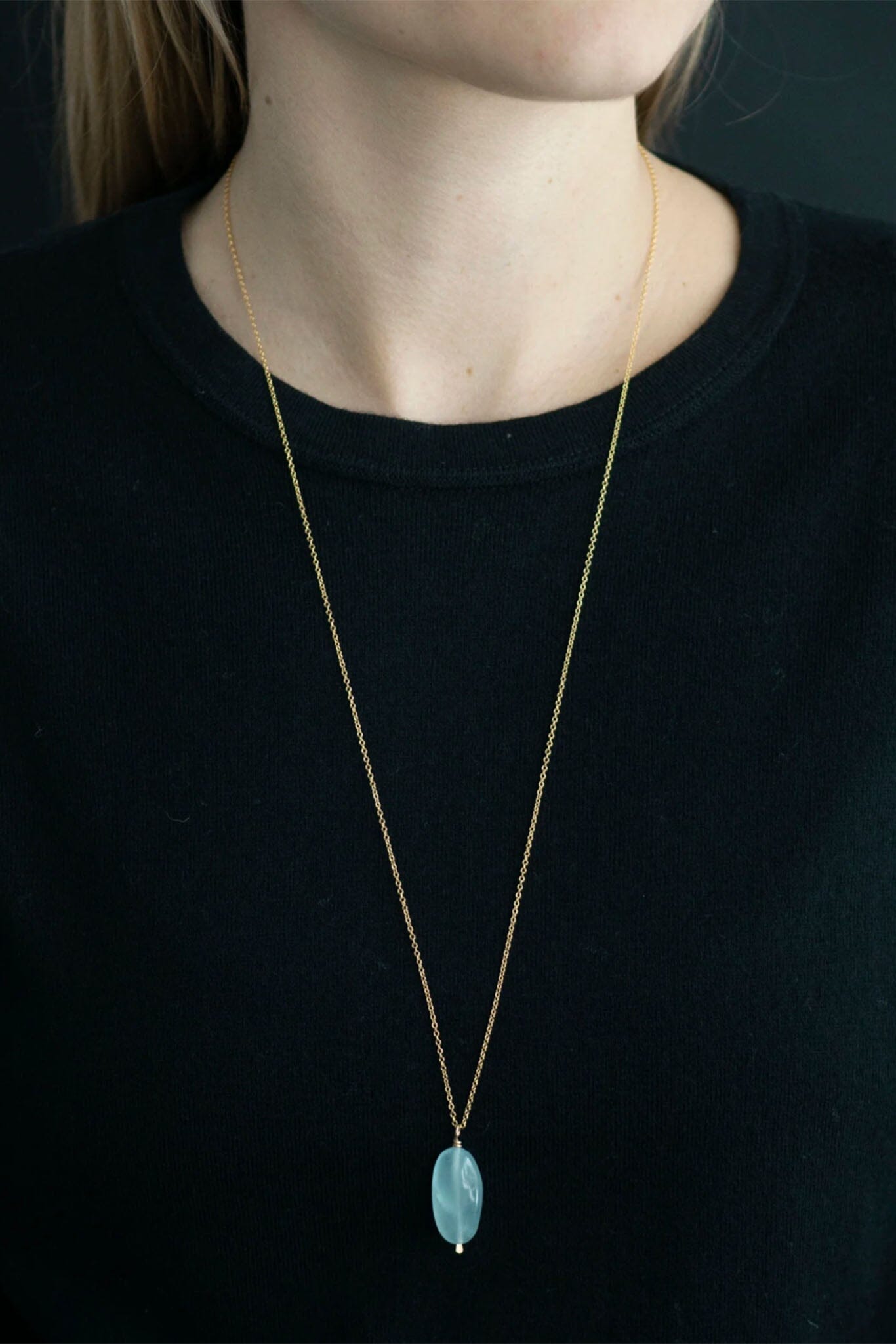 Necklace with an aquamarine pendant worn by a person against a black background