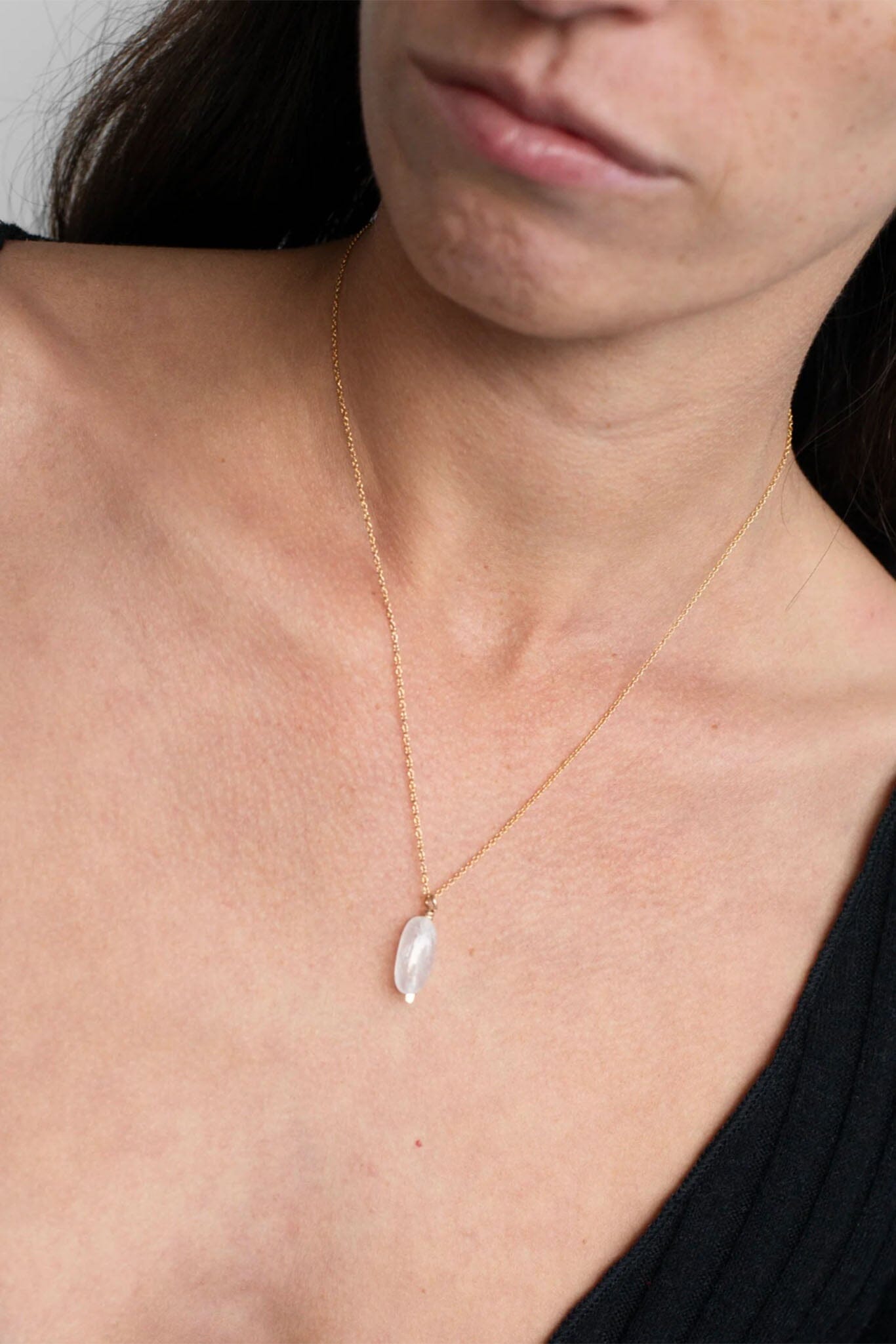 Close-up of a woman wearing a gold necklace with a moonstone pendant.