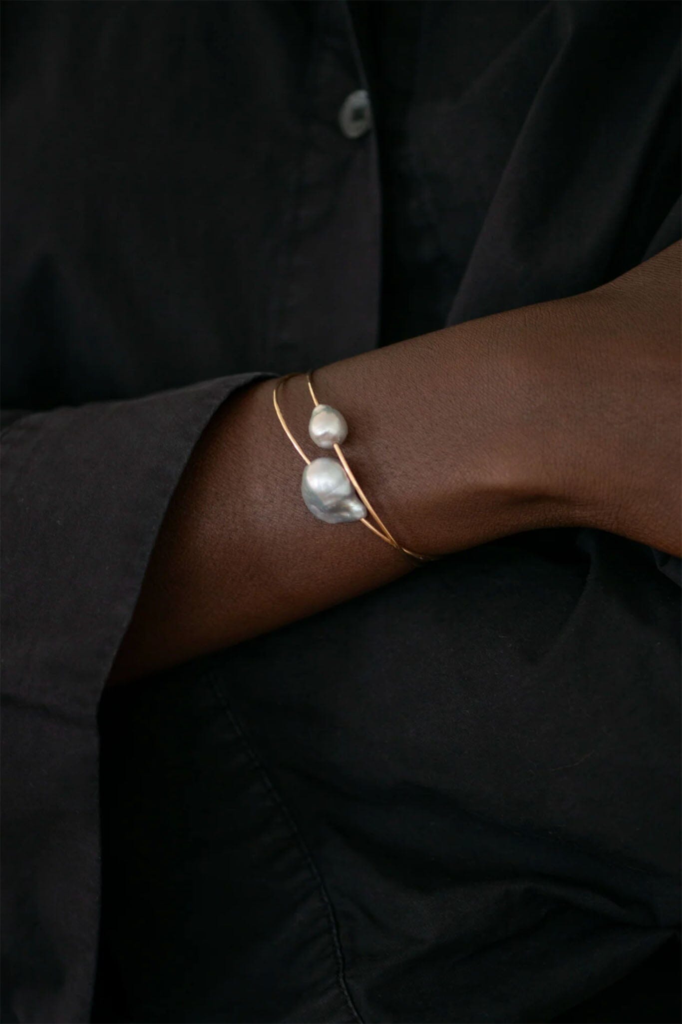 Close-up of a wrist wearing a gold bracelet with a pearl on a dark background