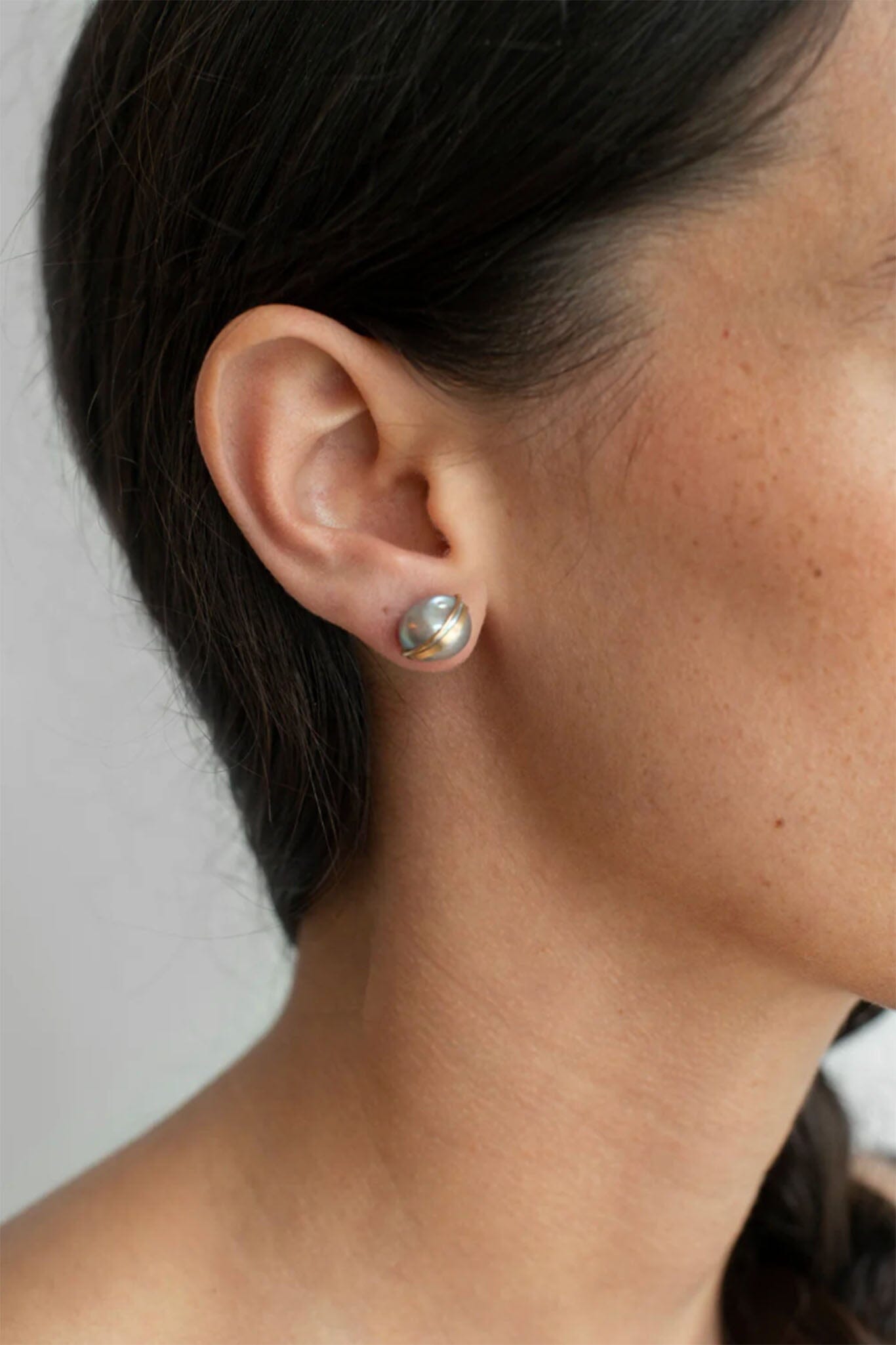 Close-up of an ear wearing a pearl earring with a neutral background