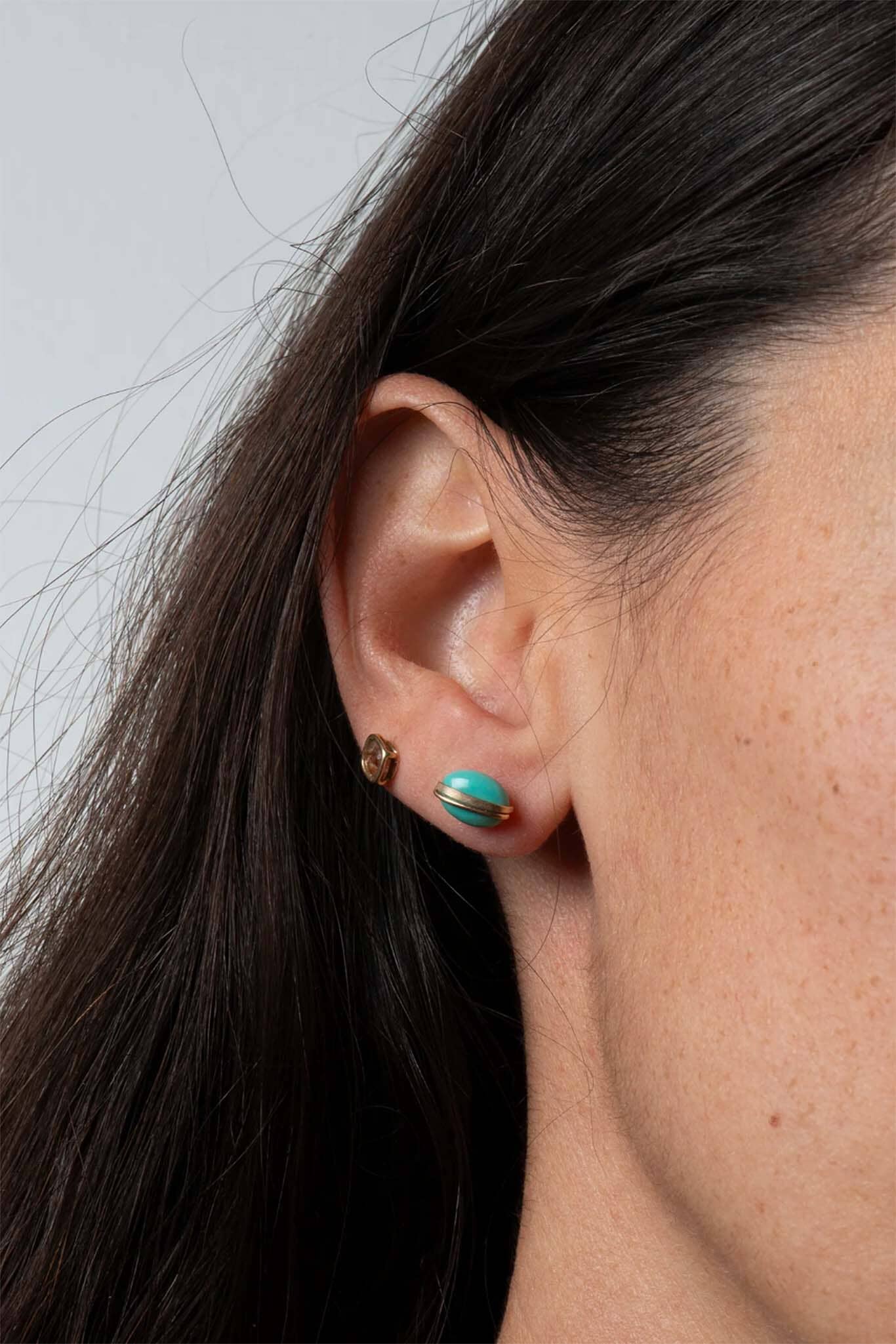 Close-up of an ear wearing turquoise earrings with a neutral background