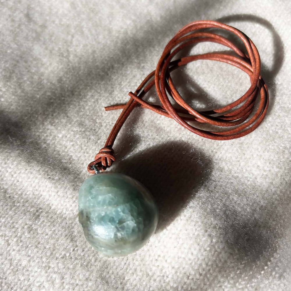 Green round stone on a brown cord against a textured gray background