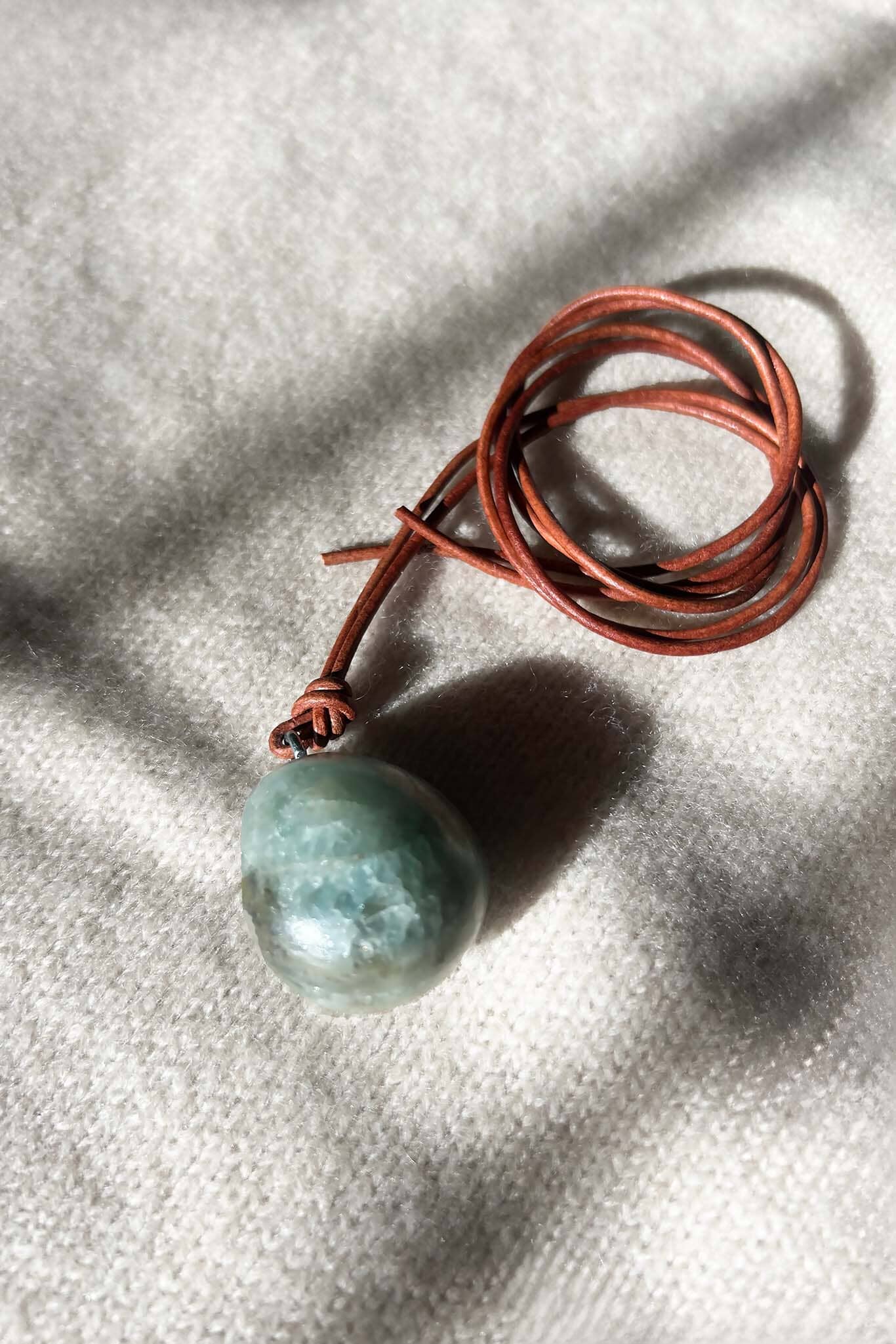 Green round stone on a brown cord against a textured gray background