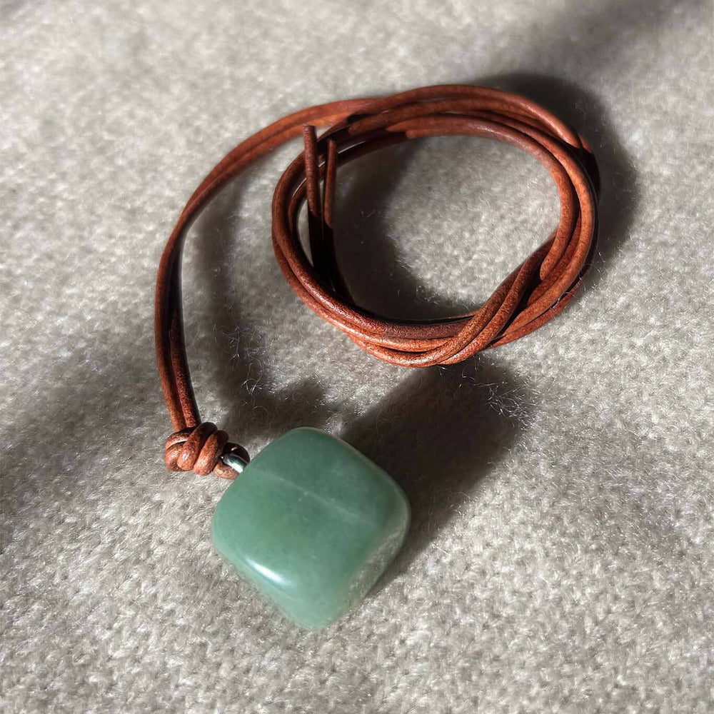 Green aventurine square pendant on a brown leather cord against a gray background