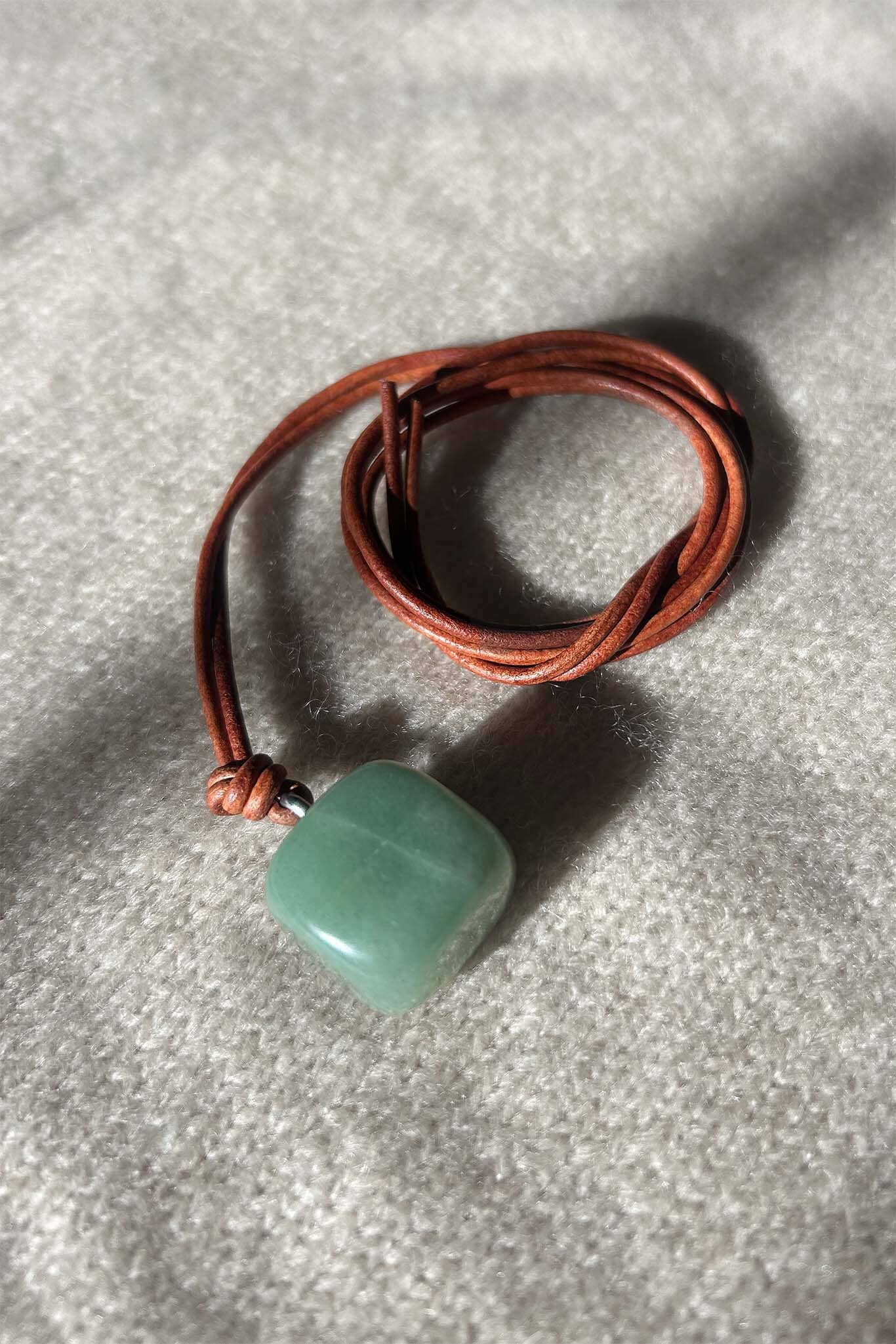 Green aventurine square pendant on a brown leather cord against a gray background