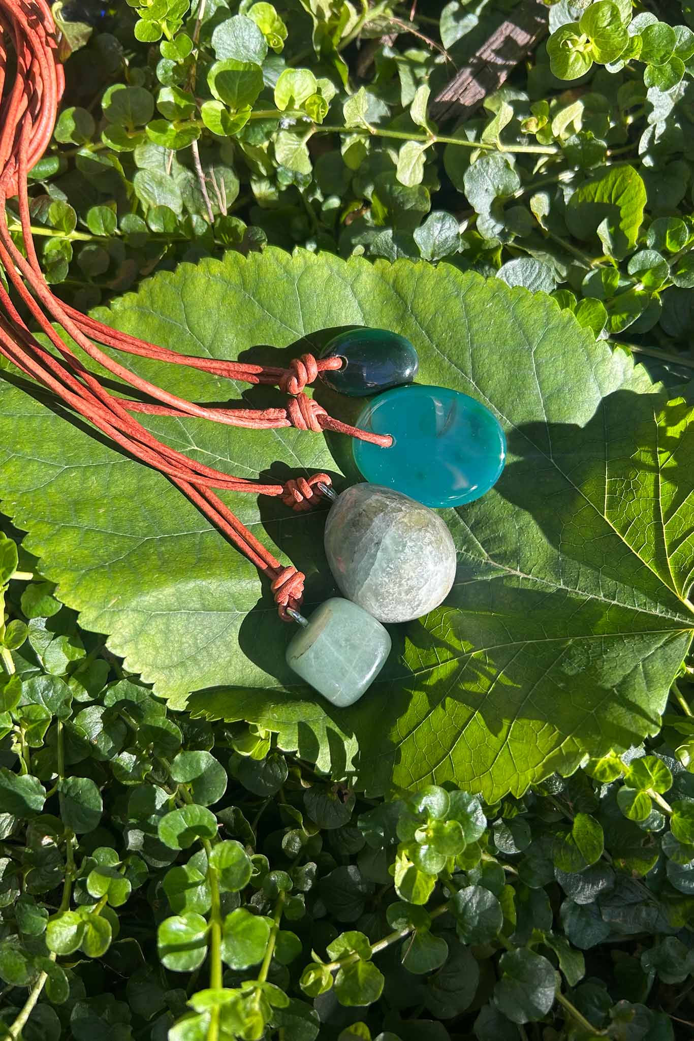 Cord necklaces with turquoise and green jade beads resting on a green leaf