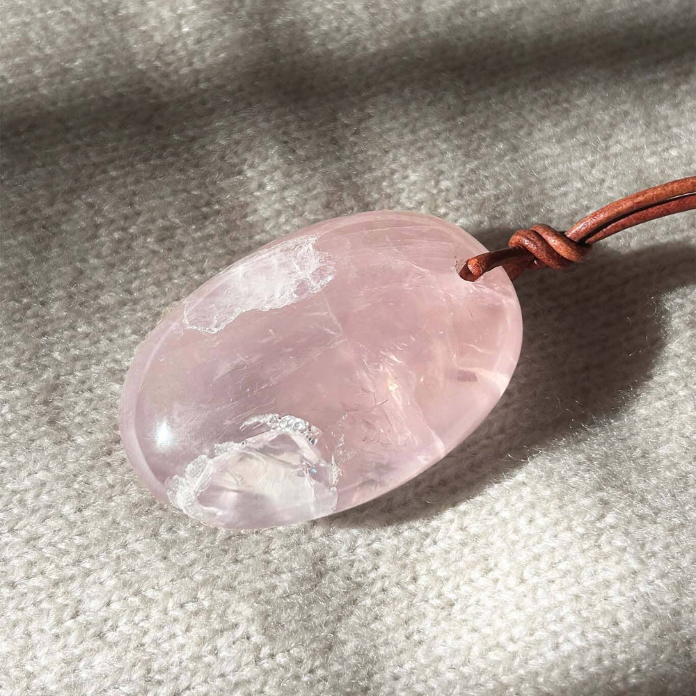 Large rose quartz pendant on a leather cord against a textured fabric background