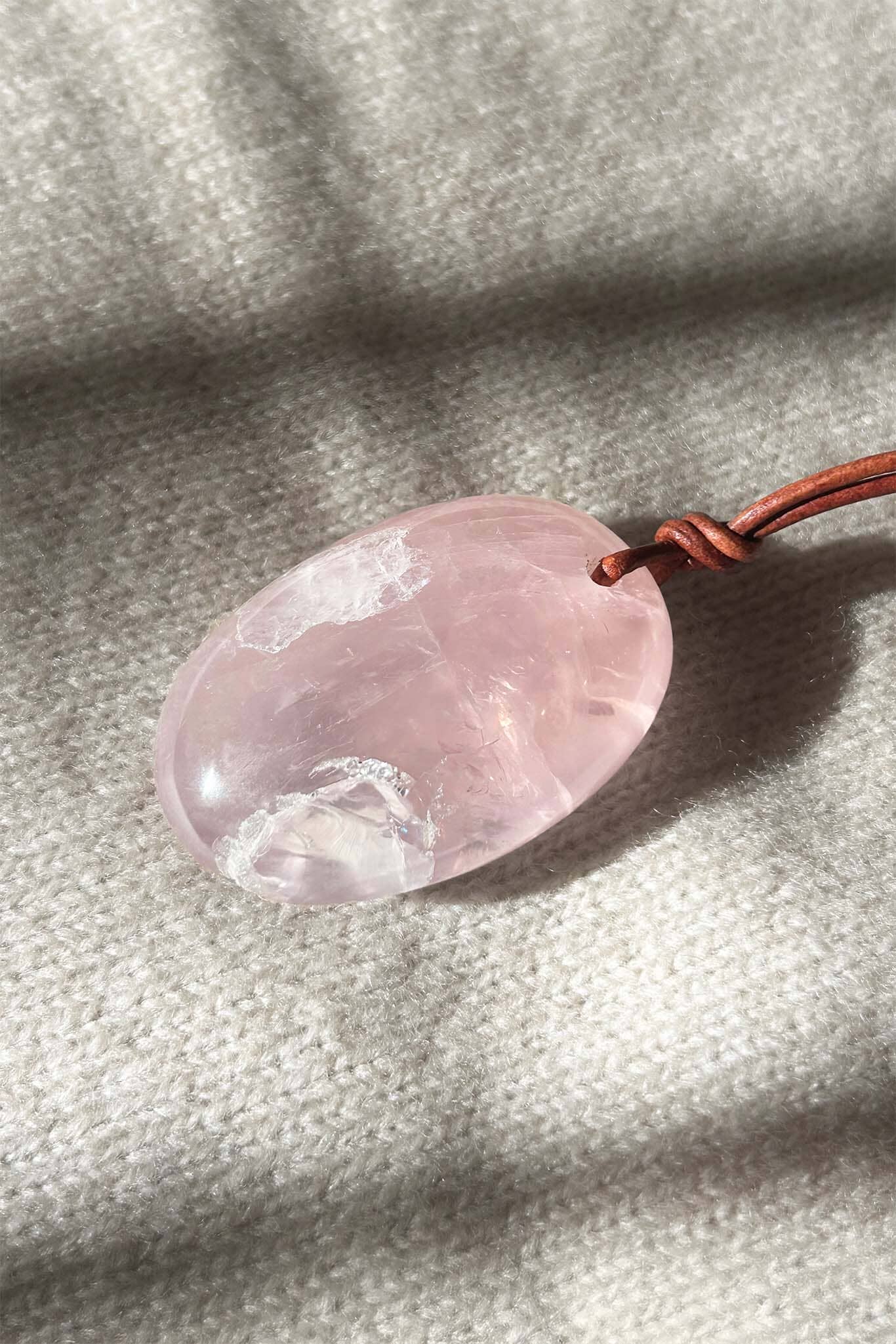 Large rose quartz pendant on a leather cord against a textured fabric background