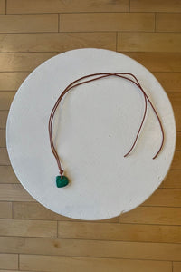 Necklace with a green malachite pendant on a white circular platform on a wooden floor.