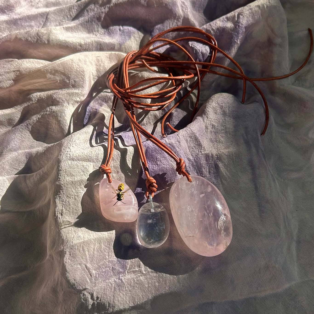 
                  
                    Necklaces with pink and clear stone pendants on a textured fabric background
                  
                