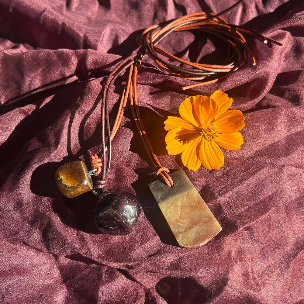 Brown stone and cord necklaces and a yellow flower on a textured purple fabric background