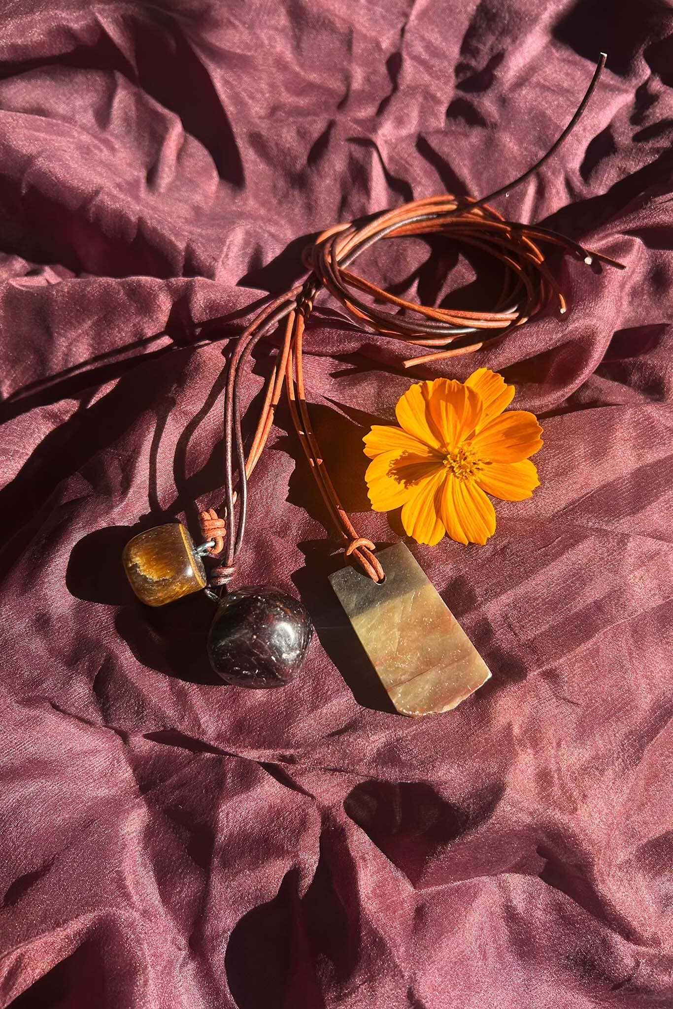 Brown stone and cord necklaces and a yellow flower on a textured purple fabric background