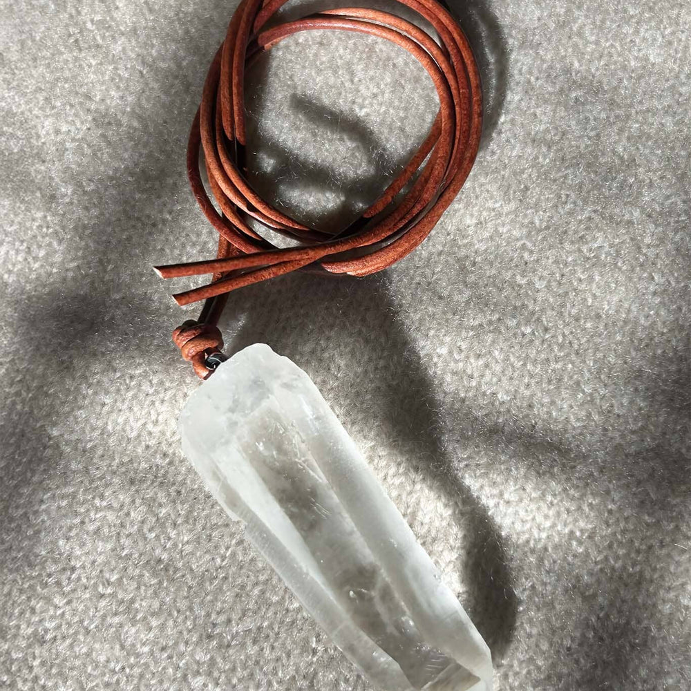 Crystal pendant on a brown leather cord against a gray background