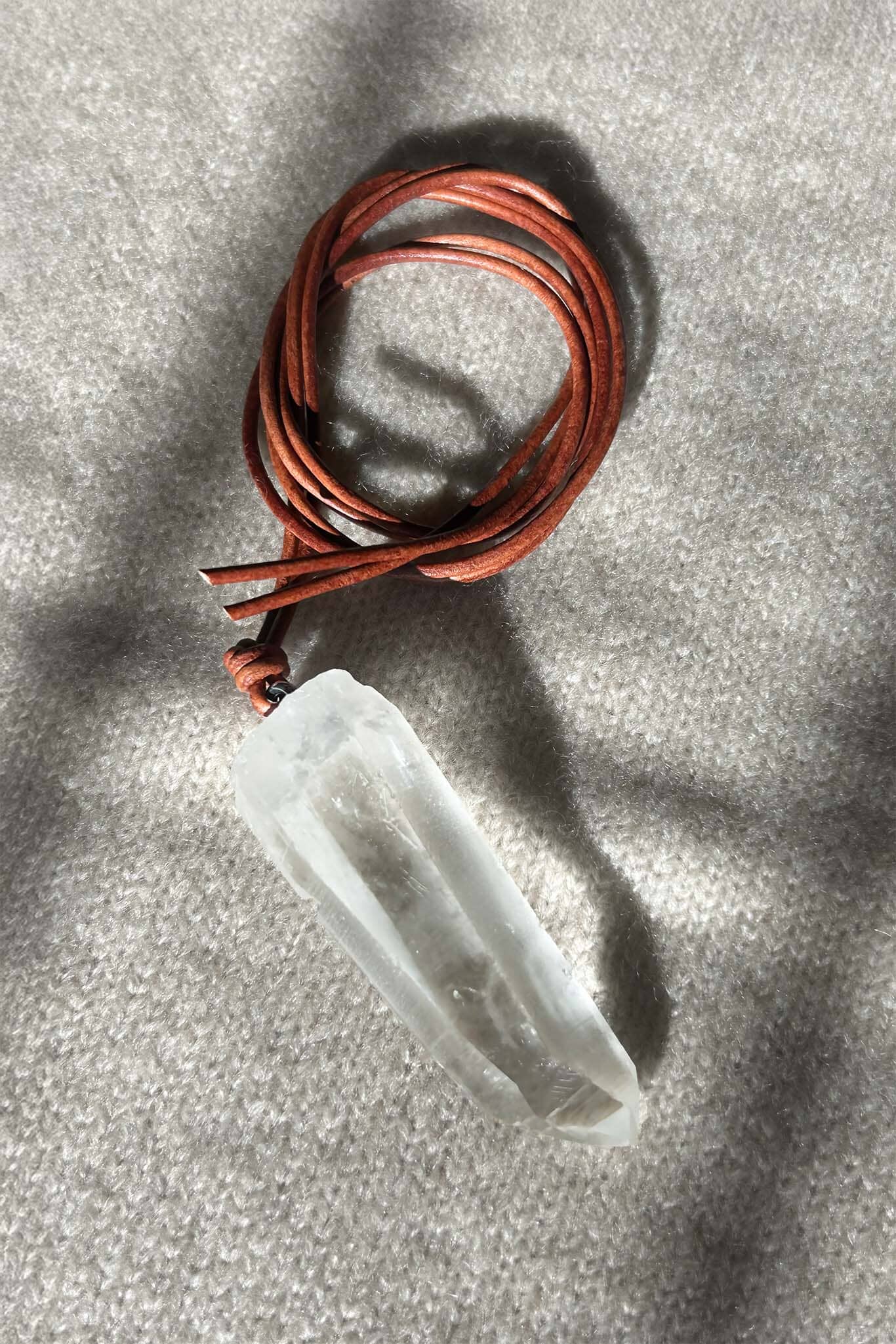 Crystal pendant on a brown leather cord against a gray background